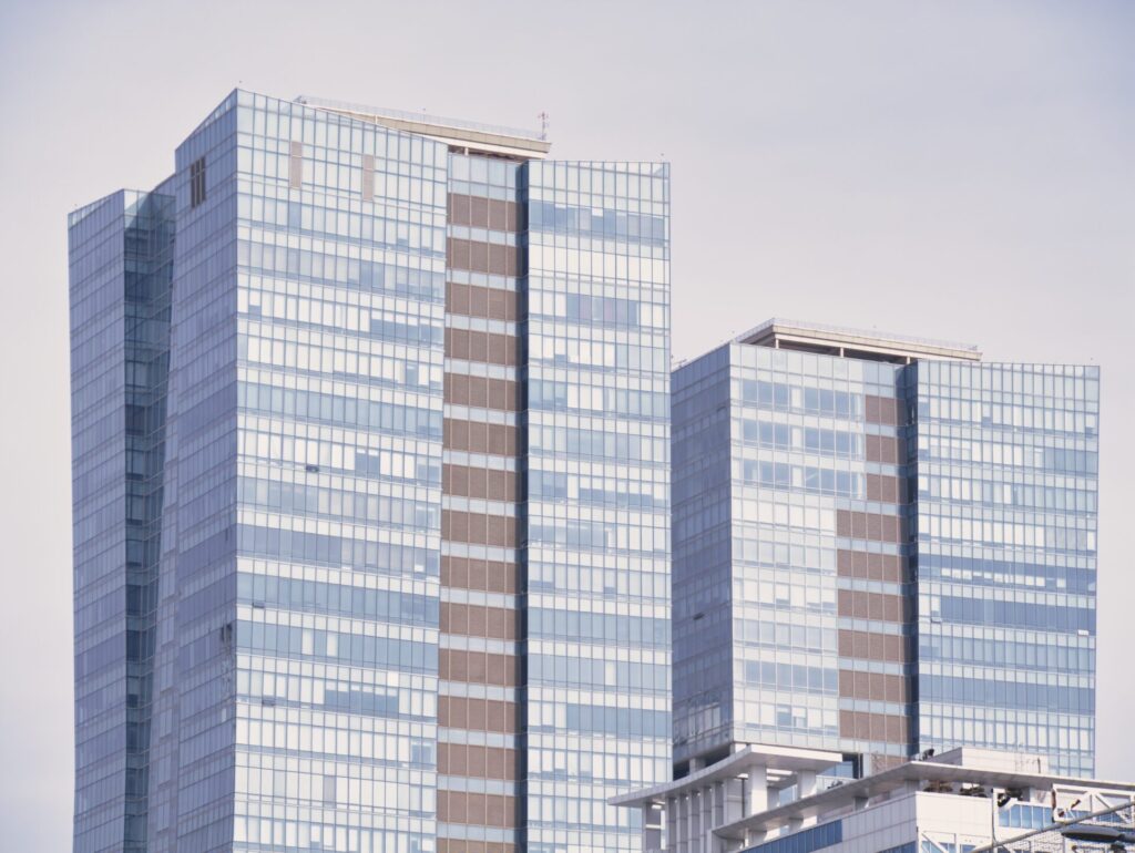 인천 송도 신도시에서 촬영한 고층 건물 풍경. 유리 외관과 세련된 수직 라인이 돋보이는 두 개의 현대식 타워가 나란히 서 있으며, 맑은 하늘 아래 반사되는 빛이 도시의 미래지향적 이미지를 강조한다. 전면에는 흰색 구조물이 일부 보이며, 도시의 정돈된 스카이라인을 구성한다.